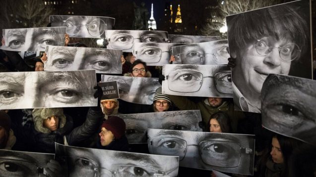 Fotos dos cartoonistas mortos pelos terroristas em Paris erguidas por manifestantes, que seguram também um cartaz com a palavra de ordem Je suis Charlie. © John Michillo | AP terroristas em Paris